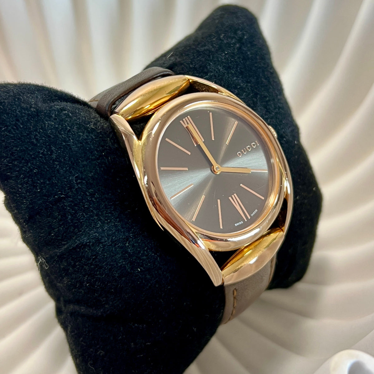 Bronze Gucci Horsebit watch with a black face on a textured white surface