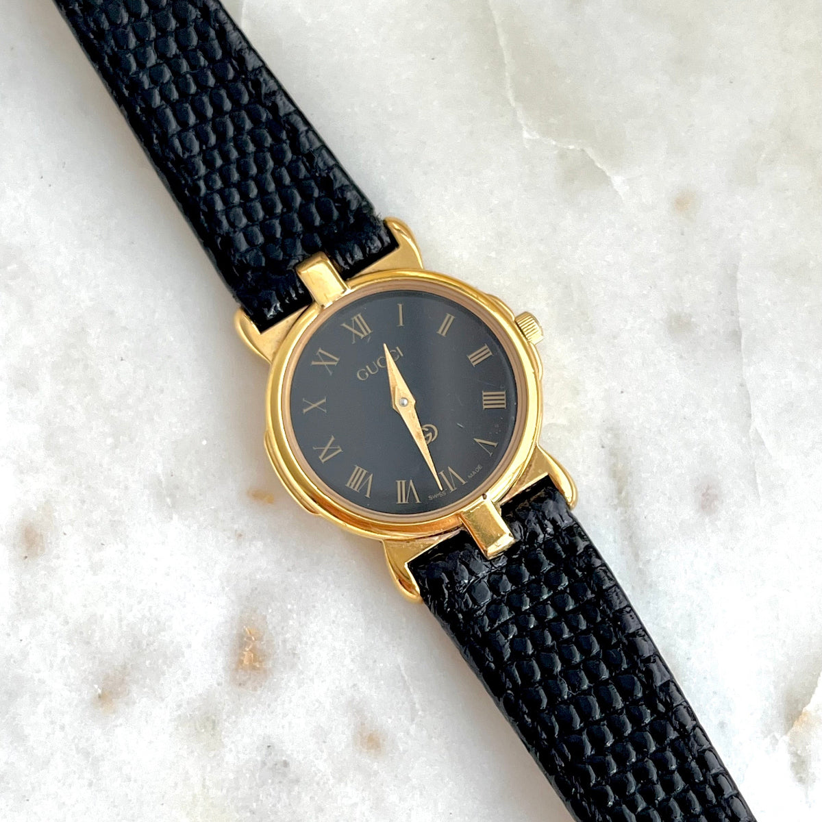 Gucci Gold Women's watch with black strap on a textured white surface