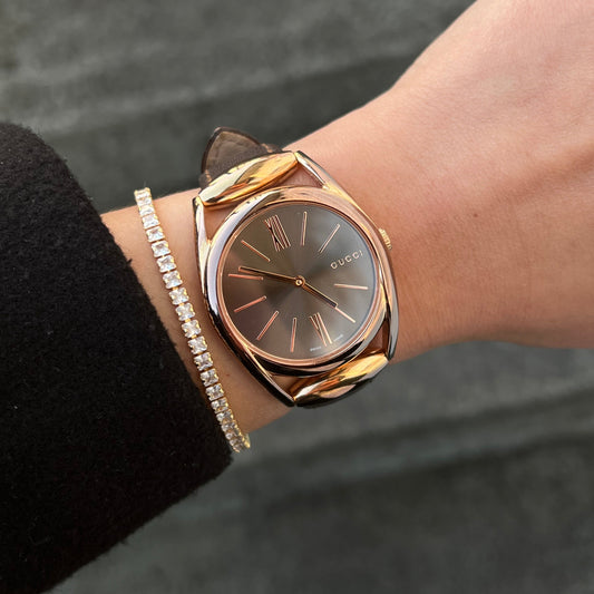 Bronze Gucci watch on a wrist with a blurred background