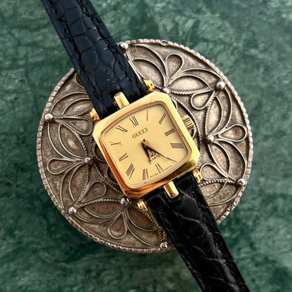 Gucci Sherry Gold watch with black leather strap on a decorative metal stand - The Gilded Hour Collection Australia NZ Collection