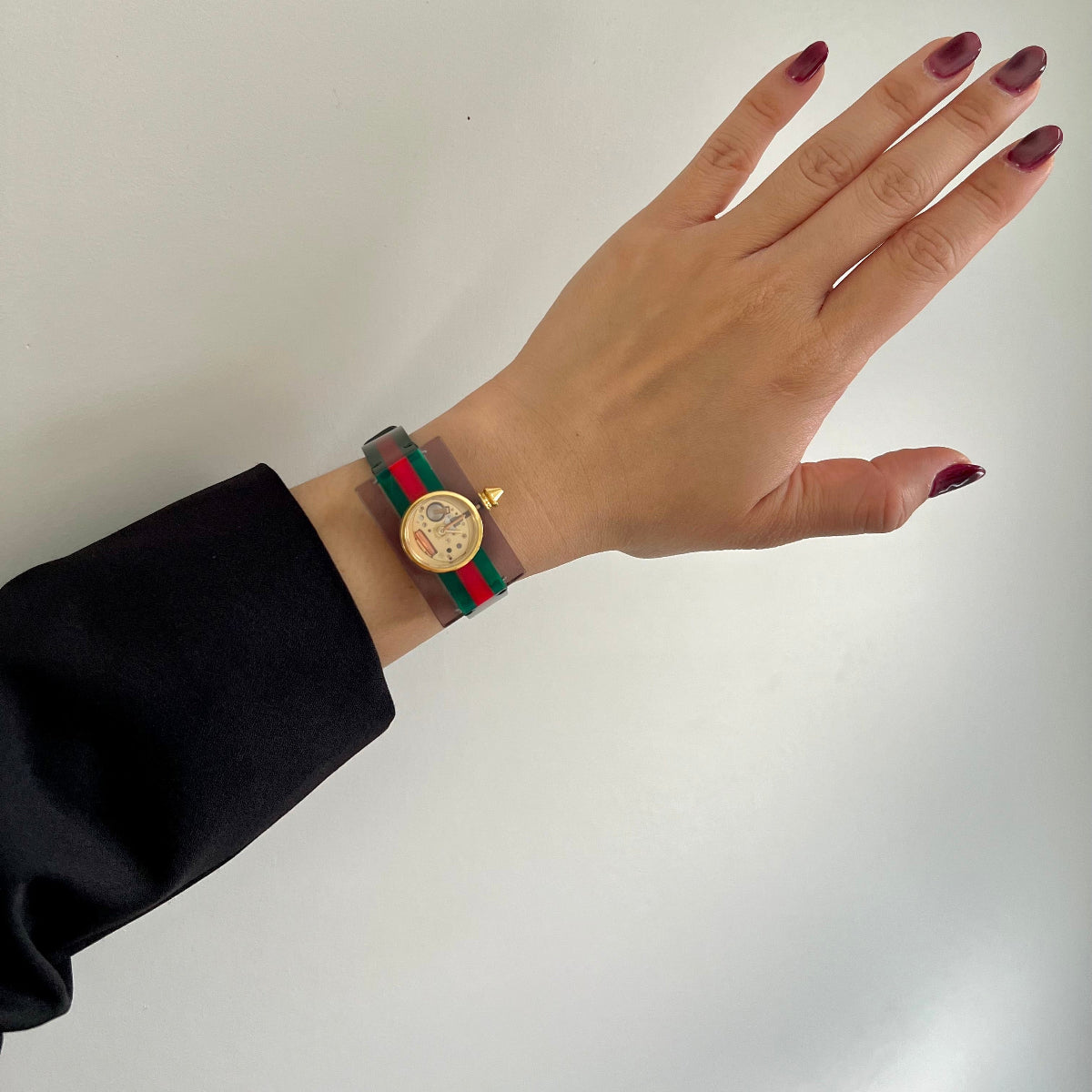 Hand wearing a Gucci Skeleton Watch with a circular watch face on a plain background