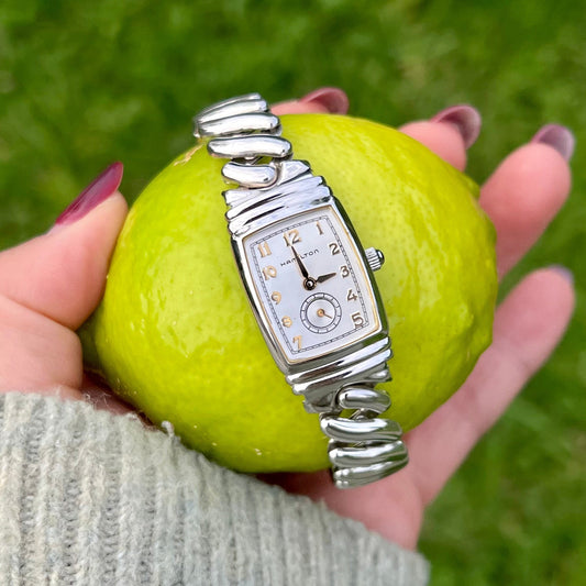 Silver Hamilton Benton women's watch on a green apple held by a hand against a grassy background