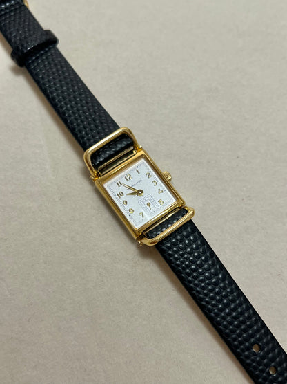 Hamilton Tank Women's watch with black strap and gold case on a beige background