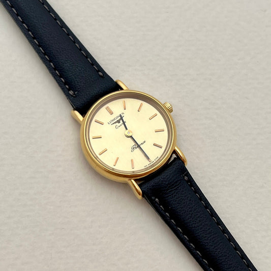 Longines Presence women's watch with black leather strap and gold case on a light gray background
