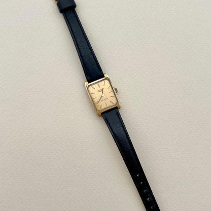 Wristwatch with black strap and gold case on a light gray background