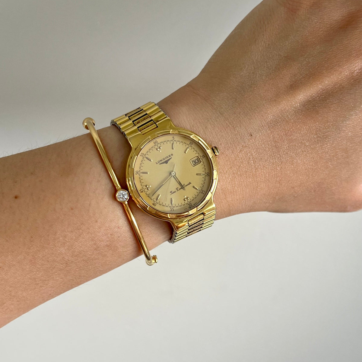 Gold LONGINES wristwatch on a wrist with a plain background