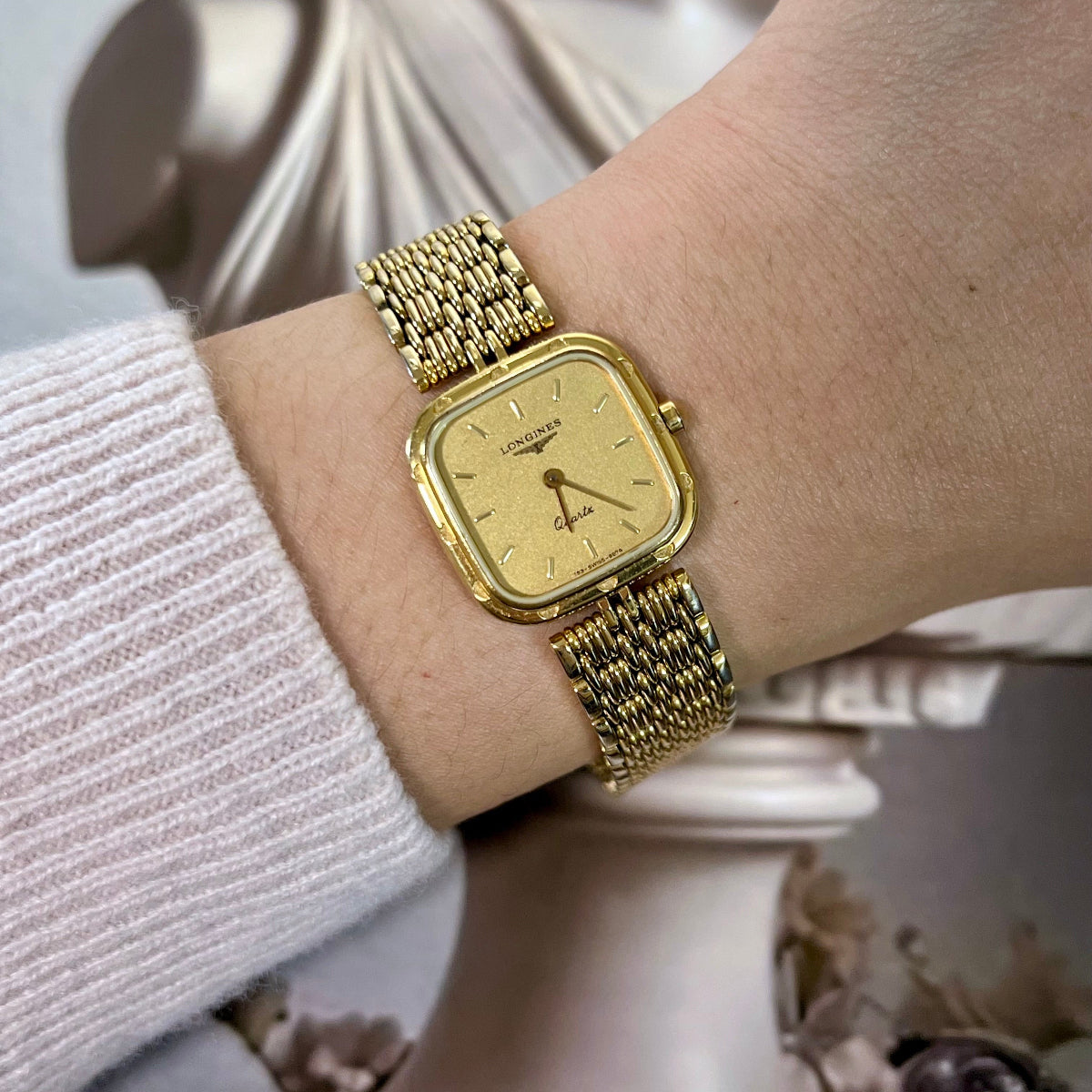 Gold wristwatch on a person's wrist with a blurred decorative background