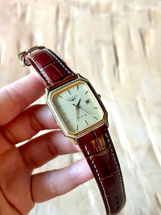 Vintage Longines watch with brown leather strap held by a hand against a neutral background