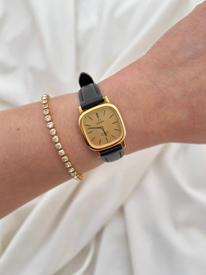 Omega Gold watch with black strap on a wrist against a white background