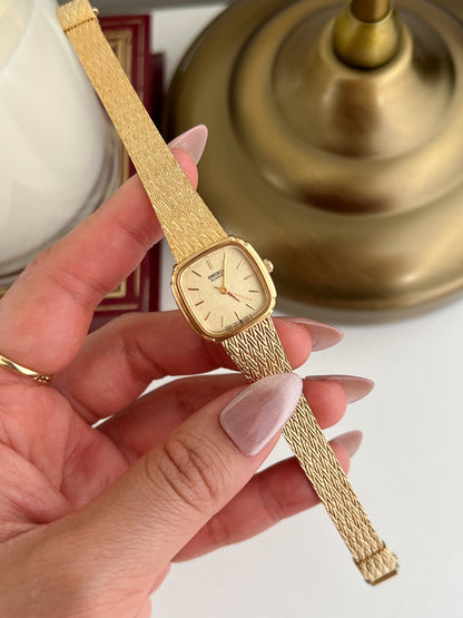 Gold Seiko Women's watch with mesh band held by a hand against a blurred background