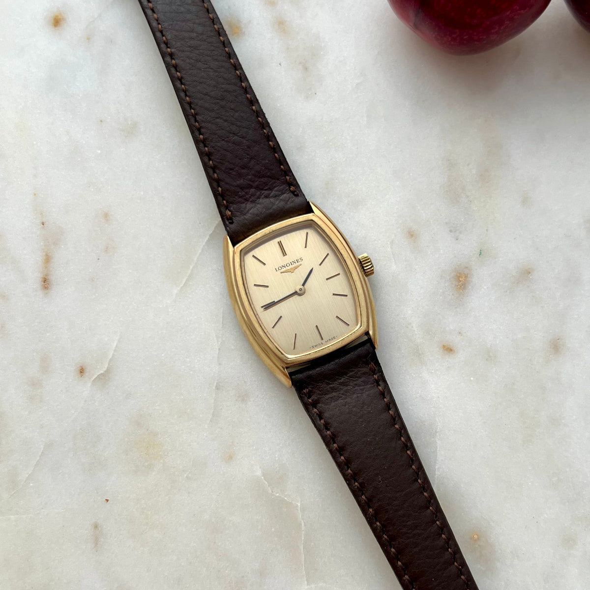 Gold Longines Women's Watch with brown leather strap on a marble surface with cherries