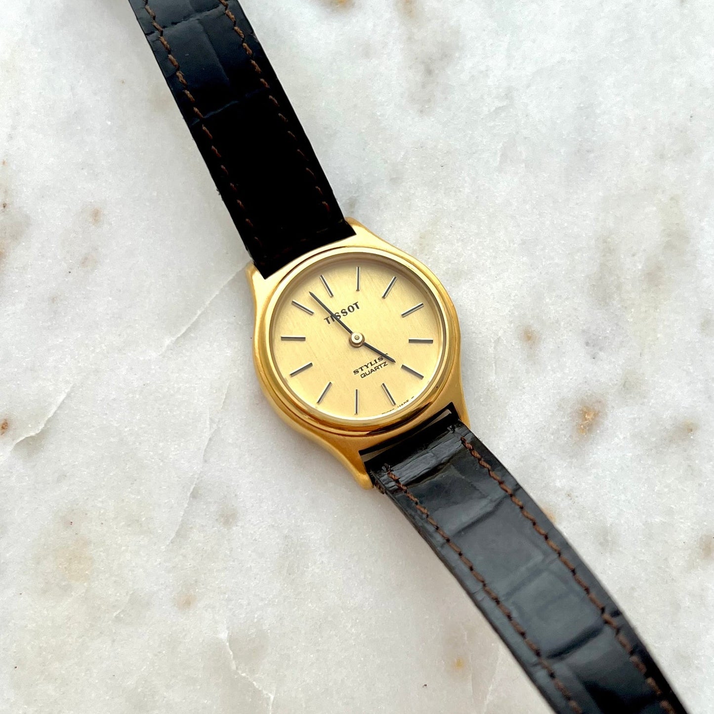 Gold watch with black leather strap on a marble surface