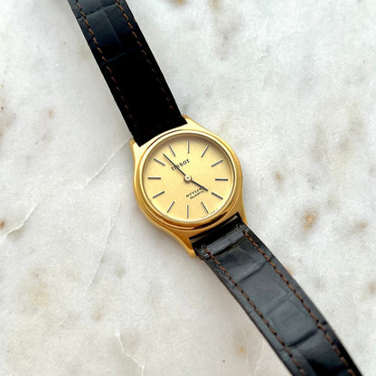 Gold watch with black leather strap on a marble surface
