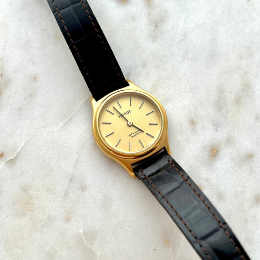 Gold watch with black leather strap on a marble surface