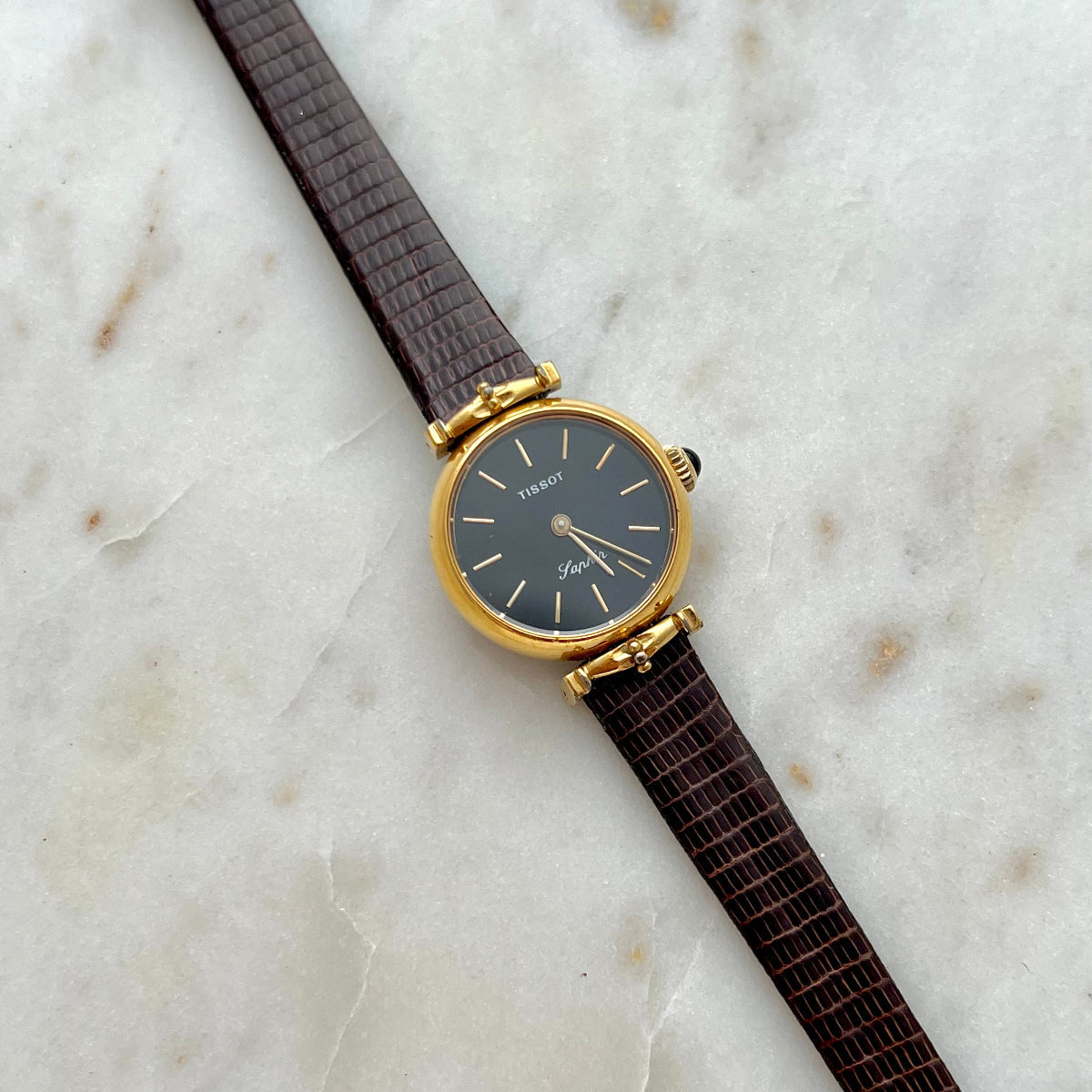 Tissot Watch with a brown strap and gold case on a marble surface