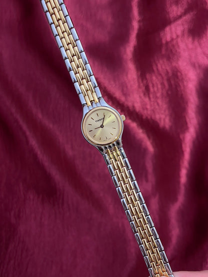 Two-tone Tissot Woman's watch NZ with gold and silver band on a maroon fabric background