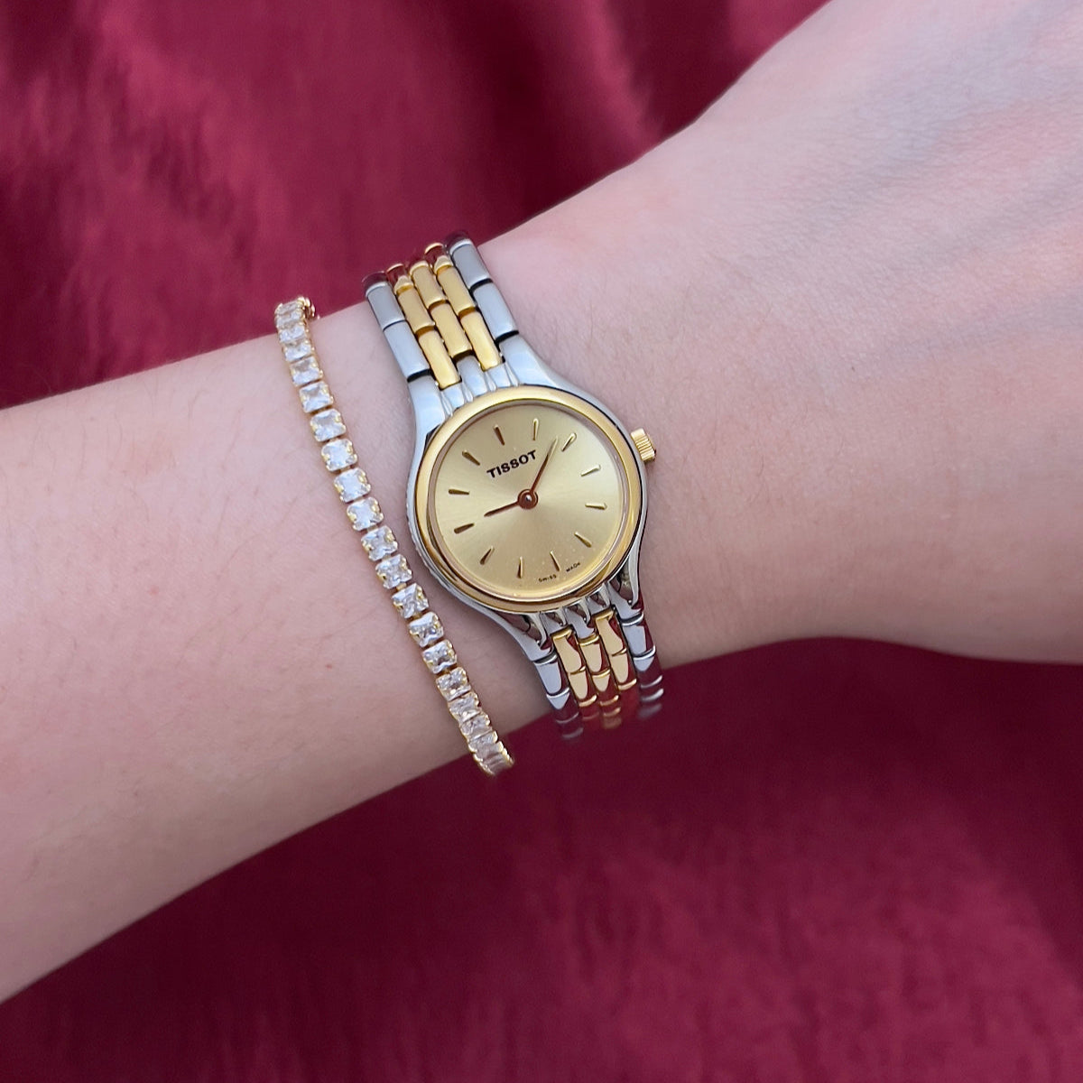 Gold Tissot watch and bracelet on a wrist against a red fabric background