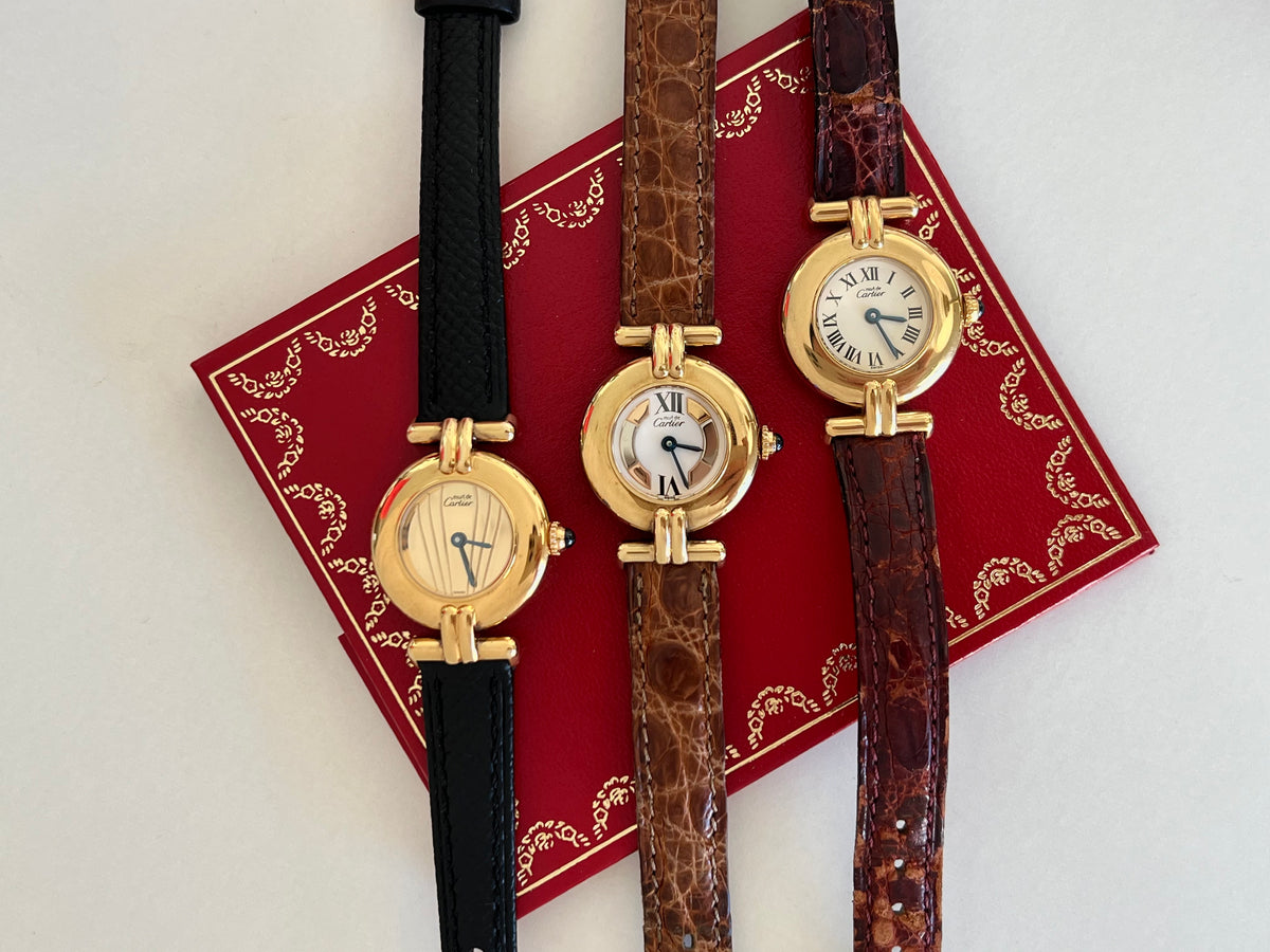 Three gold vintage Cartier women’s watches with black, brown and burgundy leather straps arranged on a red Cartier booklet