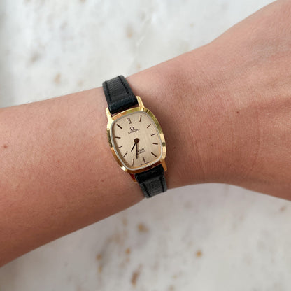 Gold watch with black strap on a wrist against a light background