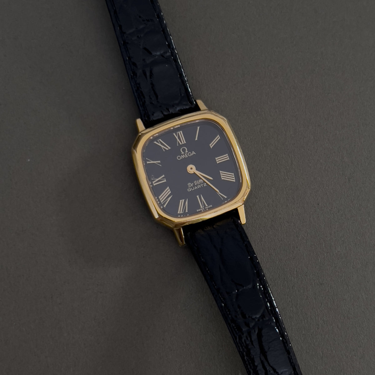 Vintage Omega luxurious woman's watch with black strap and gold case on a dark background