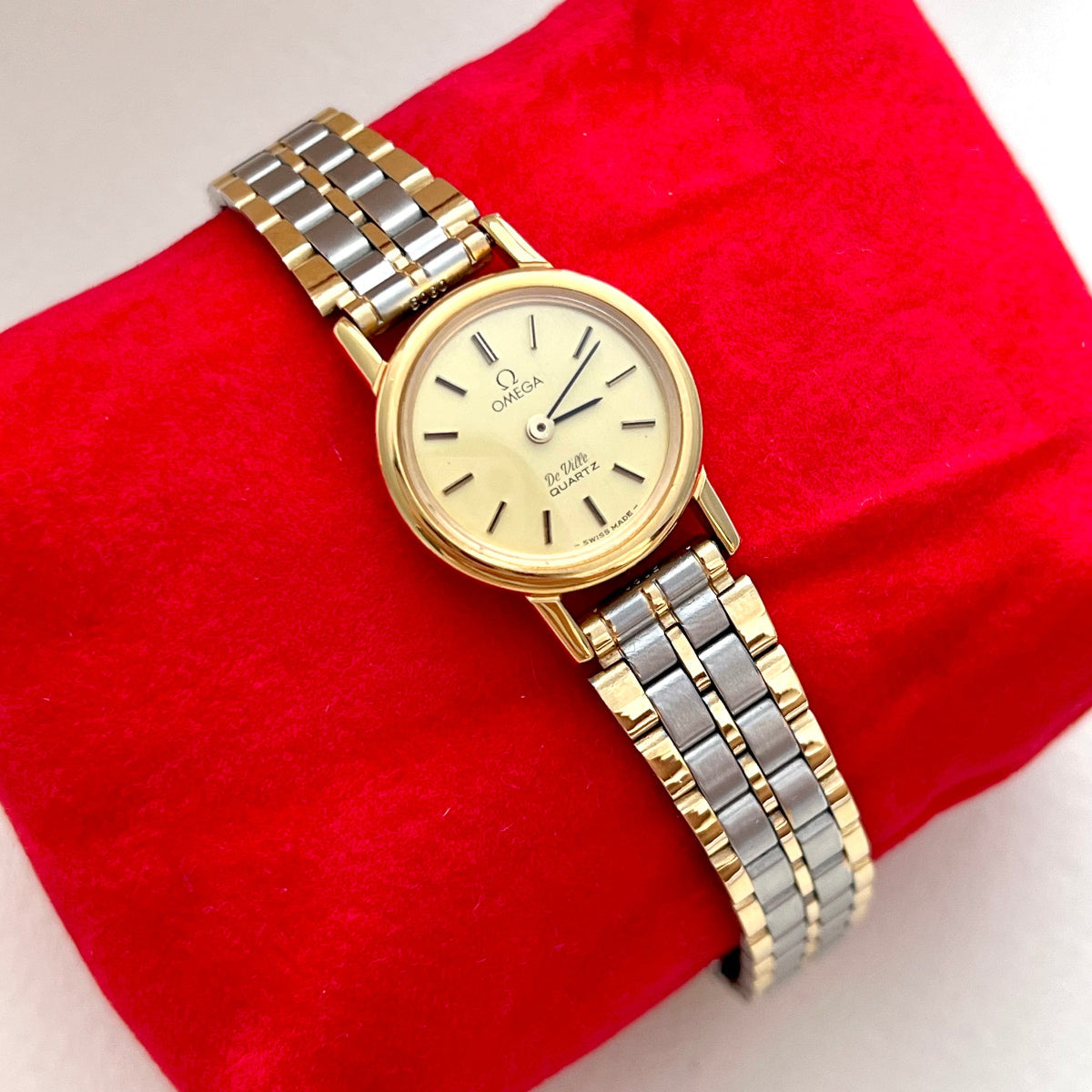 Gold and silver Omega De Ville Women's watch on a red cushion