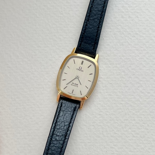 Vintage Omega tonneau watch with black leather strap on a light gray background