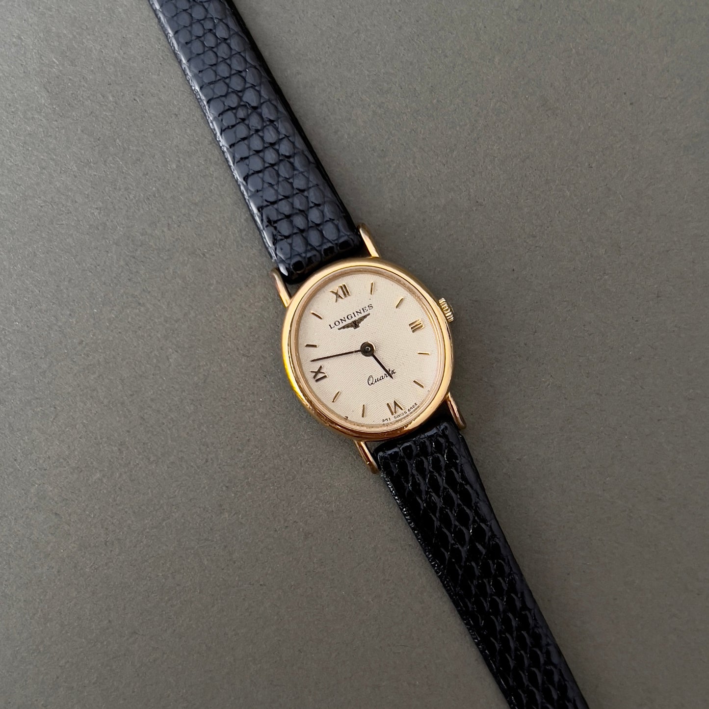 Vintage Longines Woman's luxurious wristwatch with black strap and gold case on a gray background
