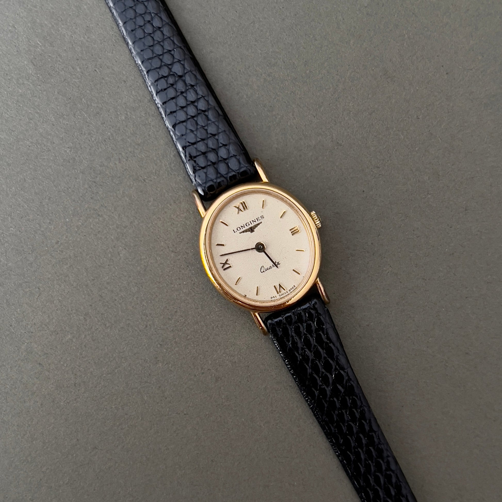 Vintage Longines Woman's luxurious wristwatch with black strap and gold case on a gray background