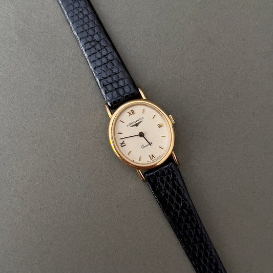 Vintage Longines Woman's luxurious wristwatch with black strap and gold case on a gray background