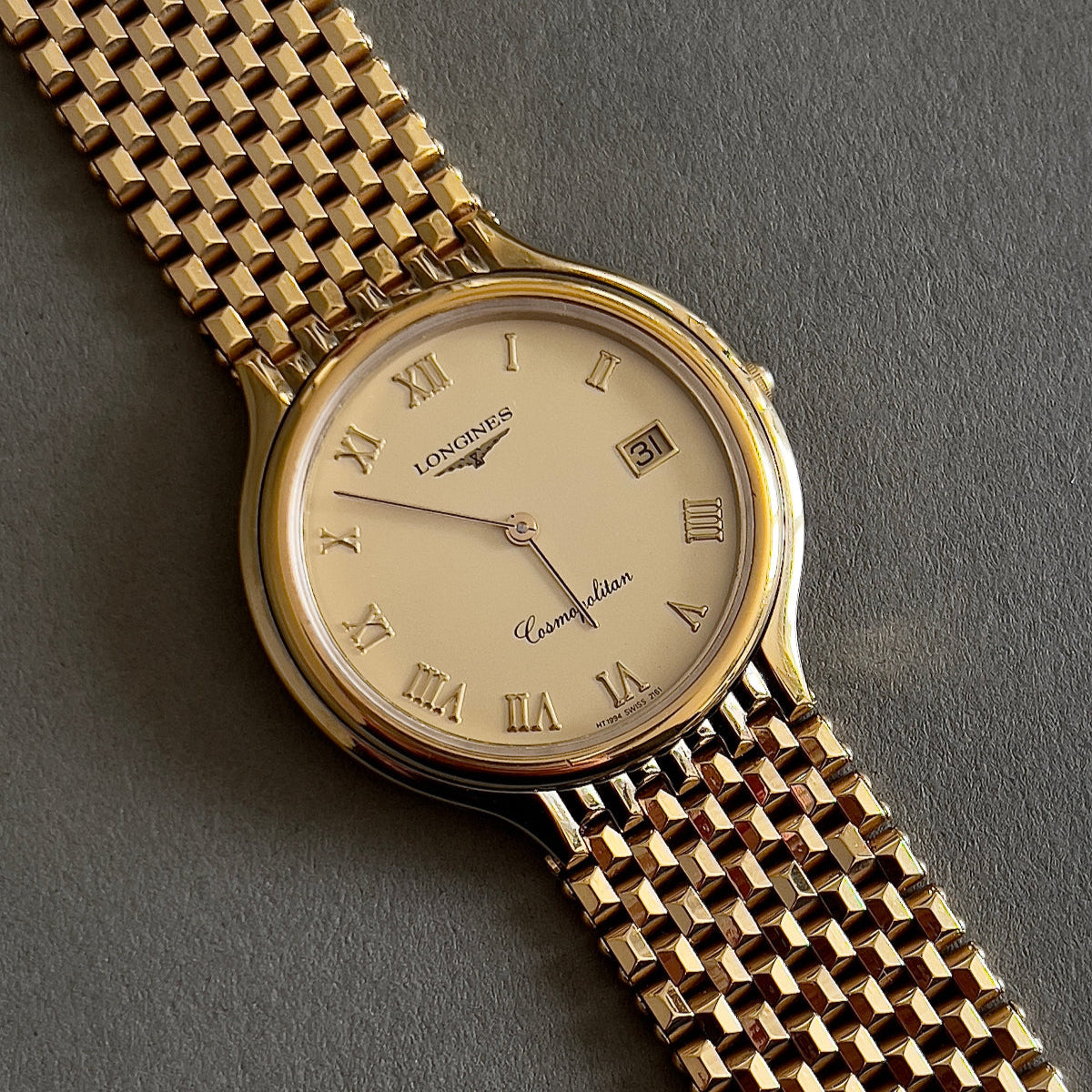 Longines gold wristwatch with a detailed face on a gray background