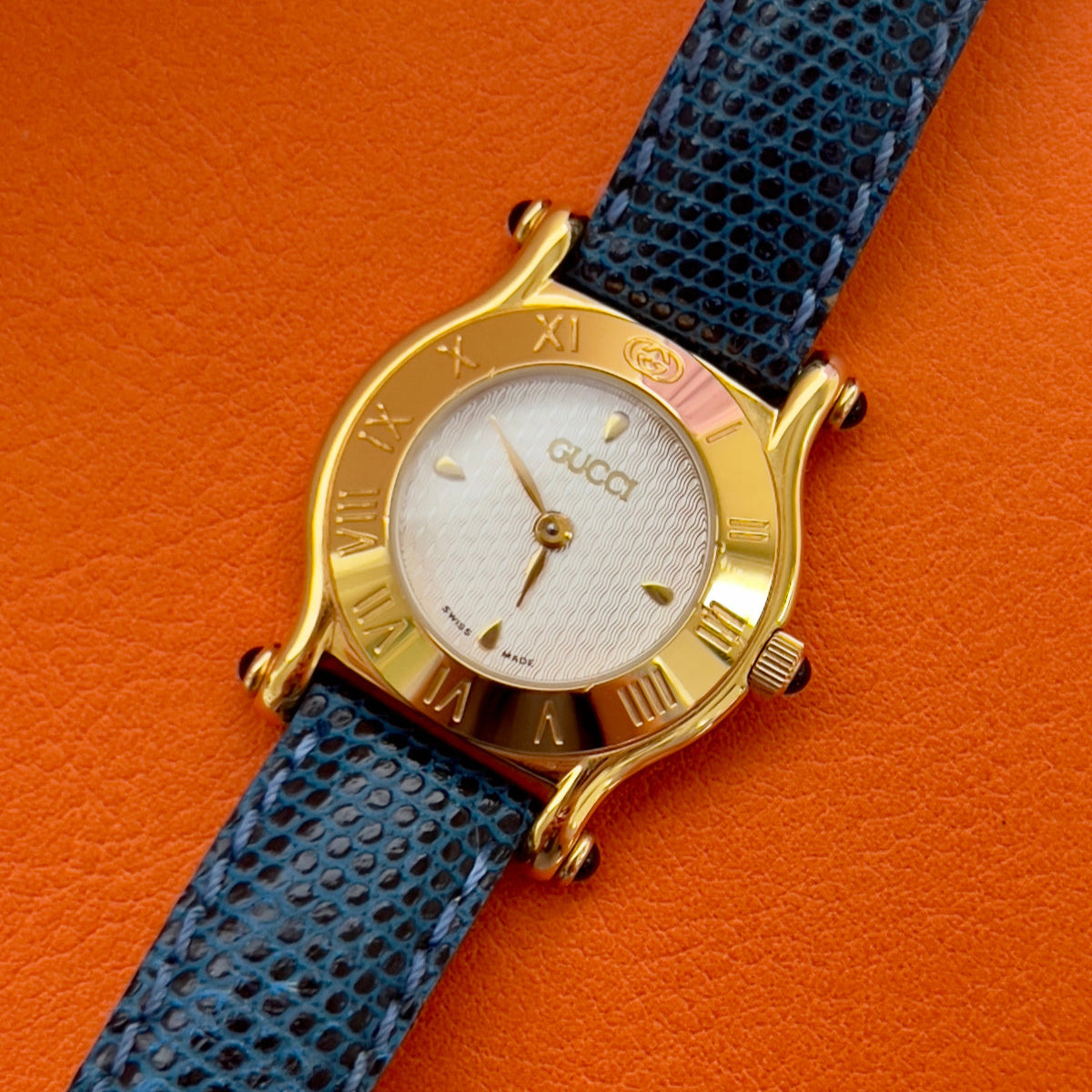 Gucci watch with blue strap and gold case on orange background