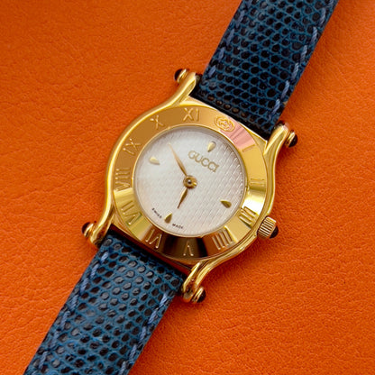 Gucci watch with blue strap and gold case on orange background