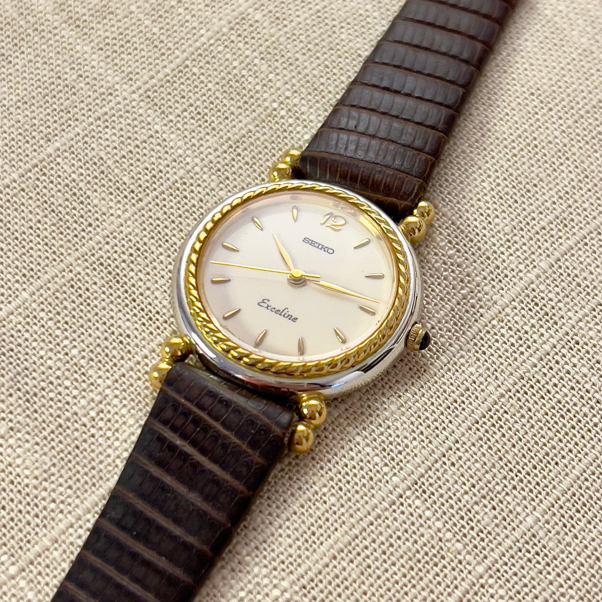 A vintage Seiko Neoclassical styled two-toned woman's watch with a gold-tone bezel and a brown leather strap, displaying a champagne dial and gold-accented lugs.