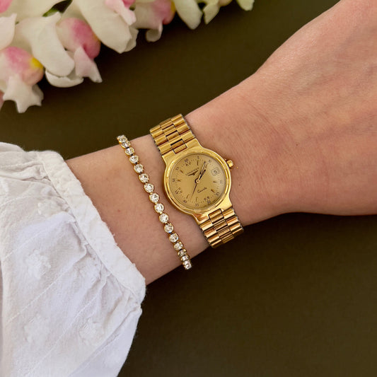 Longines gold watch and bracelet on a wrist with flowers in the background