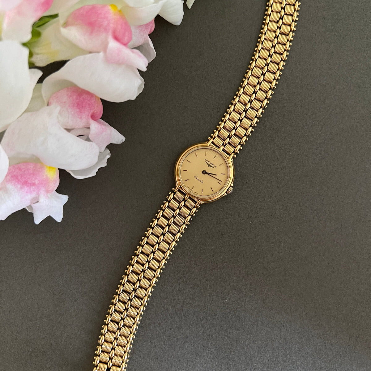Gold Longines woman's watch with a chain strap on a gray background with flowers