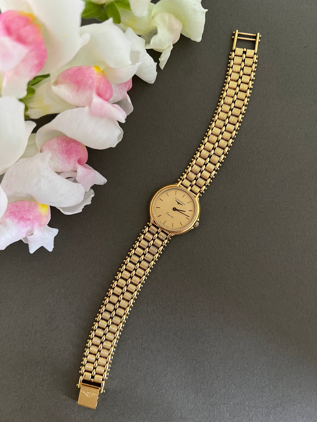 Gold Longines Swiss watch with a chain strap on a gray background with flowers