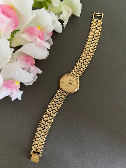 Gold Longines Swiss watch with a chain strap on a gray background with flowers