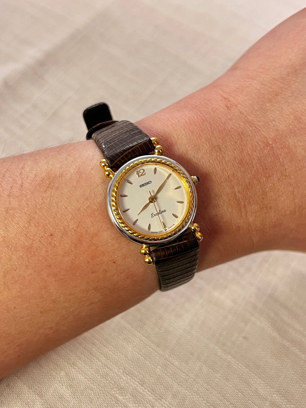Gold watch with a brown strap on a wrist against a beige background
