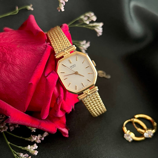 Seiko Octagonal Gold watch and ring on a dark surface with a red rose and small flowers.