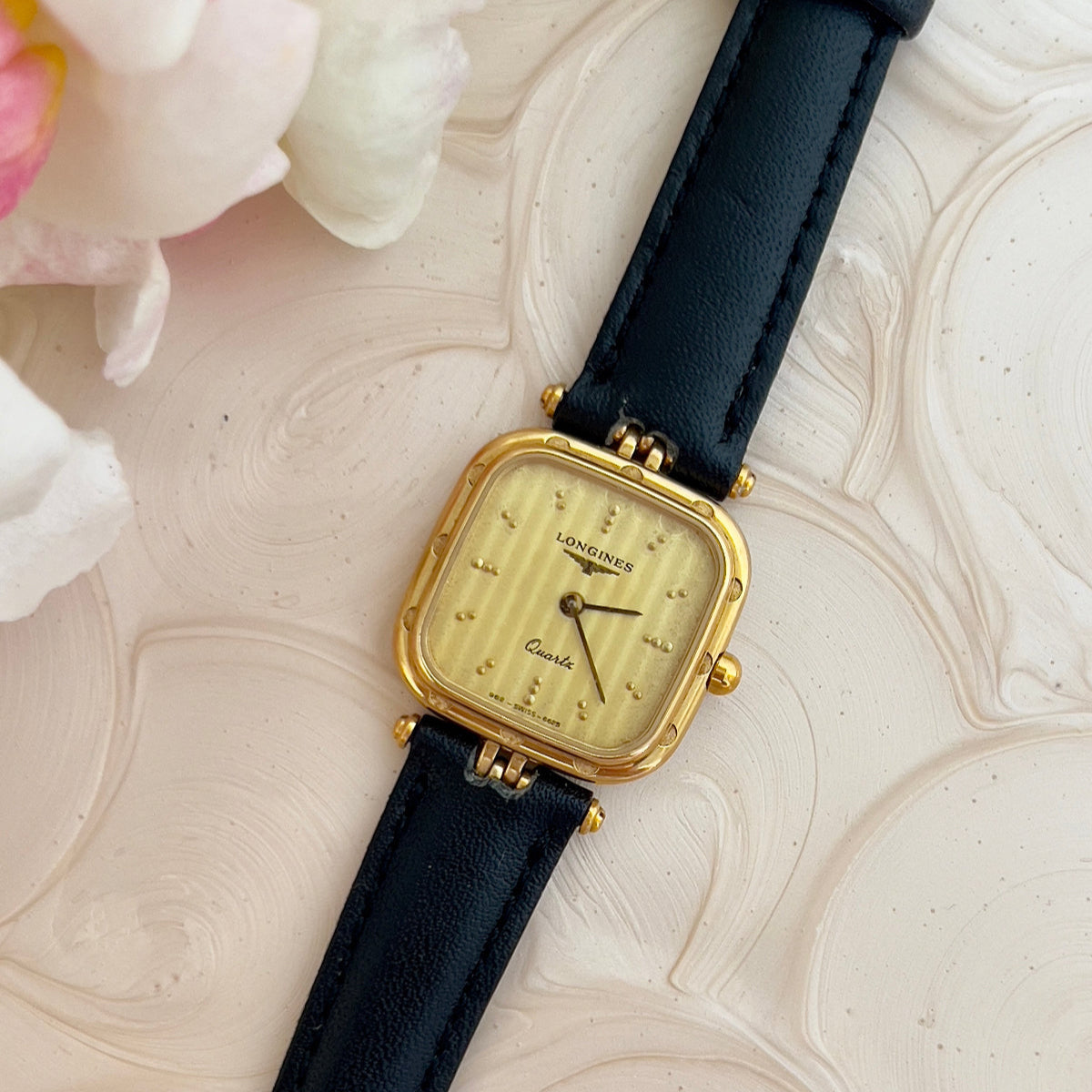 Longines gold ladies' watch with black strap on a textured surface with flowers