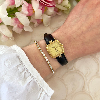Gold Longines ladies' watch on a wrist with a pearl bracelet, against a floral background