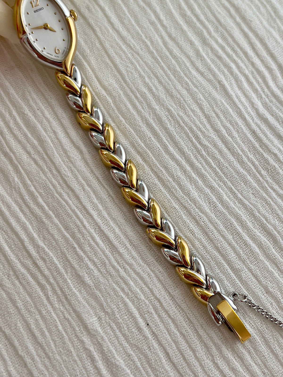 Seiko gold and silver braided bracelet on a textured beige surface