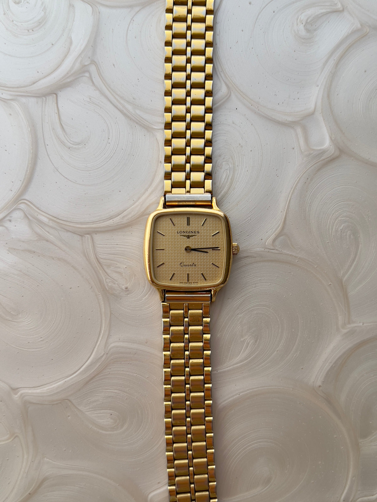 Vintage Longines gold square watch with champagne dial and waffle texture on wrist, paired with crystal bracelet.