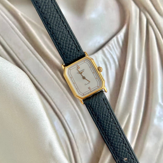 Watch with black strap and gold case on a white fabric background