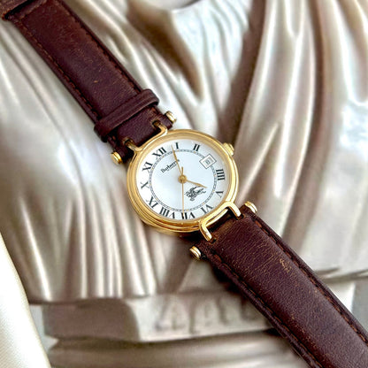 Burberry Watch with brown leather strap and gold case on a draped fabric background
