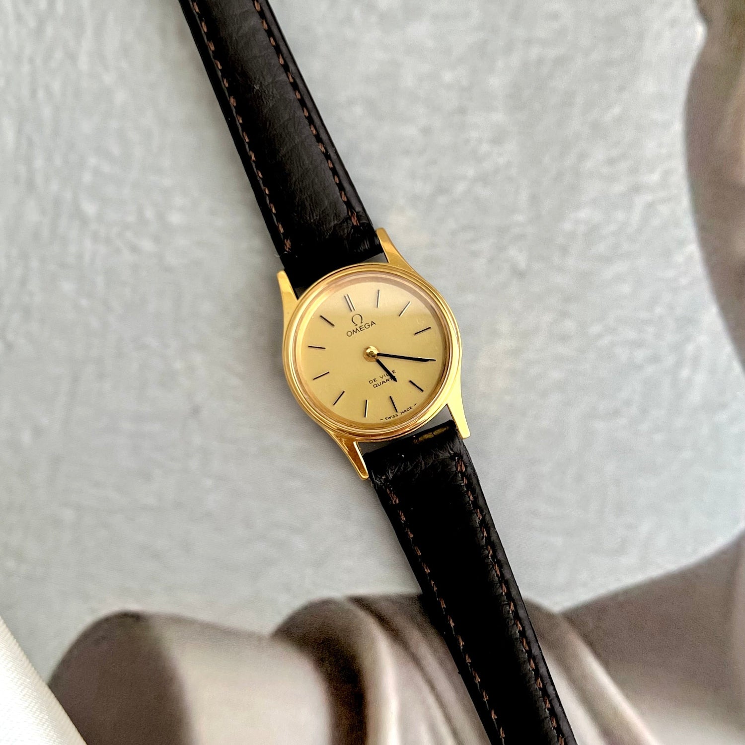 Vintage Omega De Ville watch with gold case and black leather strap on a light gray background