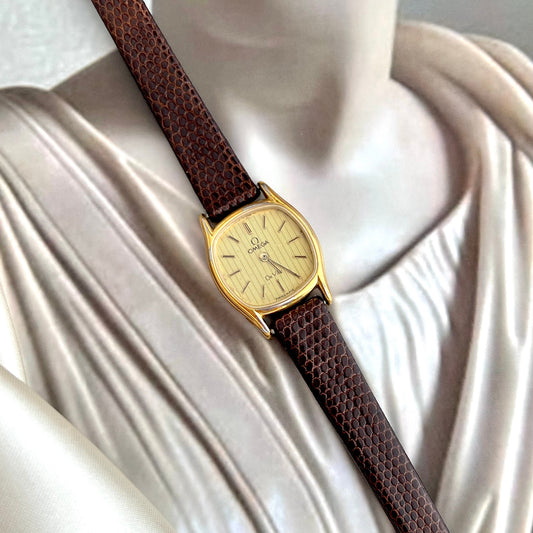 Gold Omega De Ville Women's watch with brown strap on a draped white fabric background