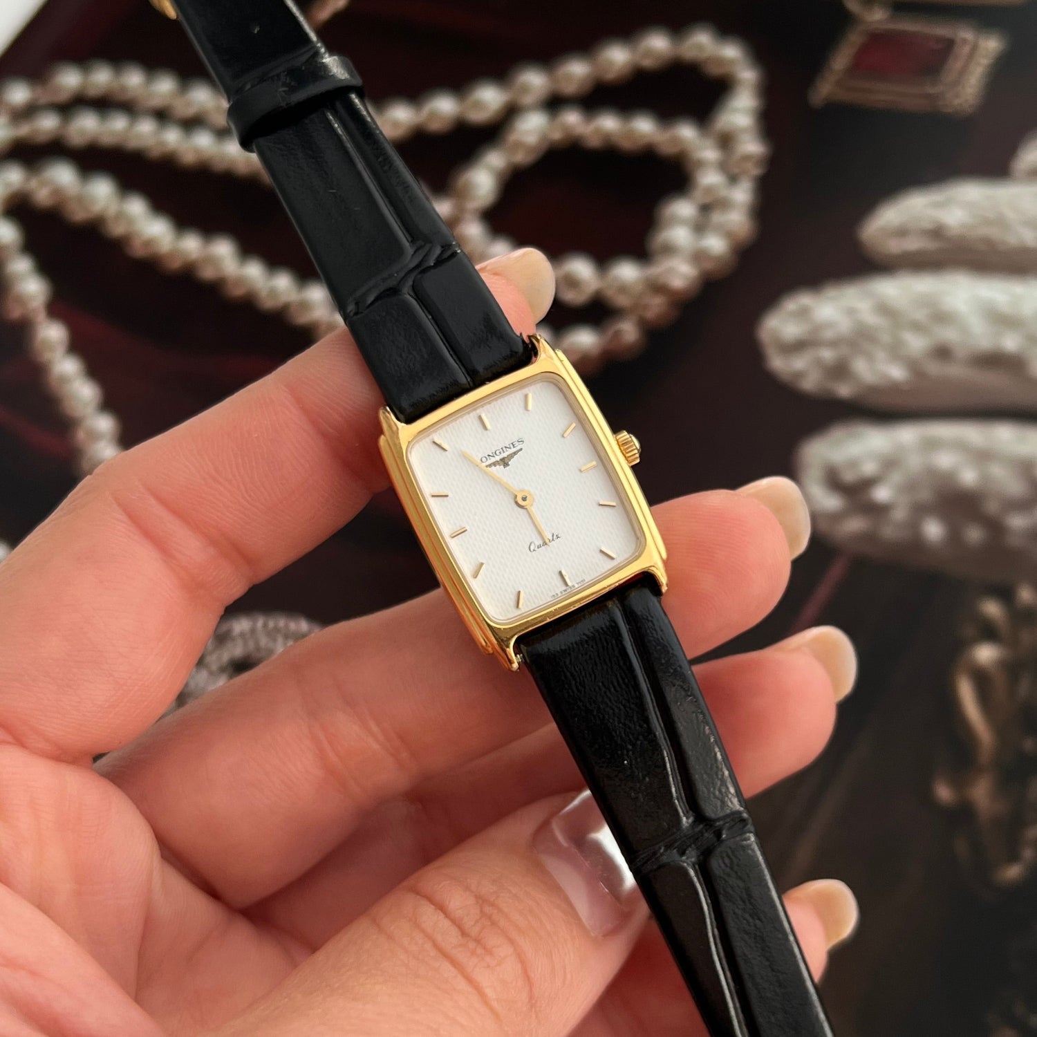 Longines Soft Tank Watch black and gold watch with a blurred jewelry background