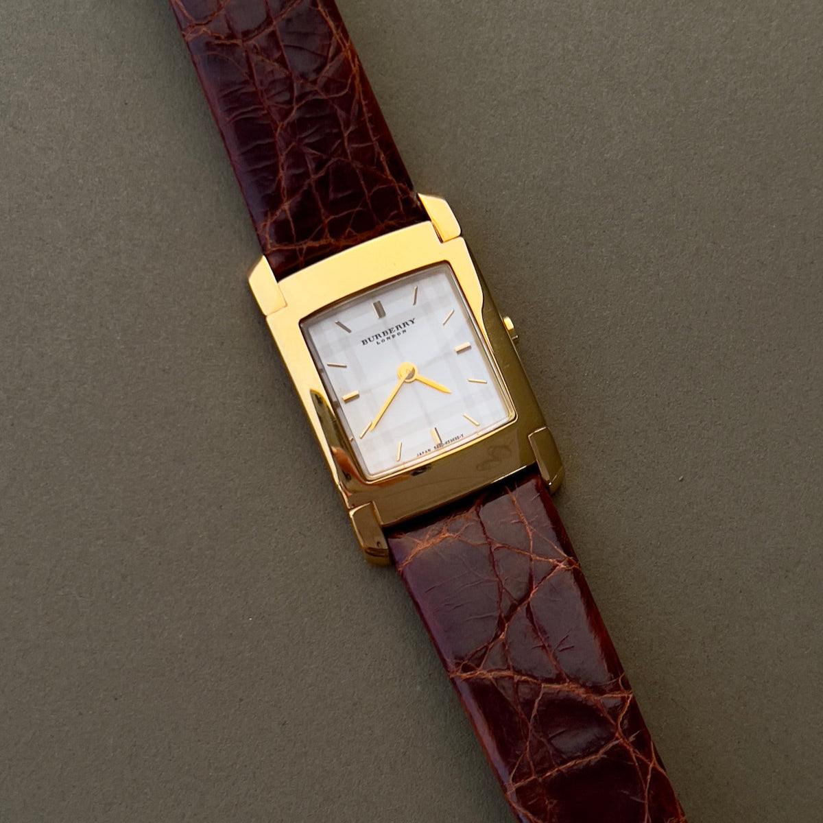 Burberry London rectangular gold ladies watch with white dial and brown croc-embossed leather strap, displayed on neutral background.