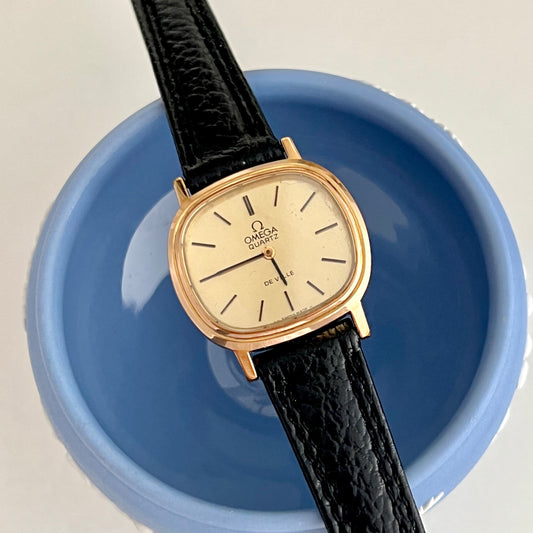 Omega De Ville Cushioned Gold watch with black leather strap on a blue dish